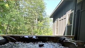 A hot tub with water jets, surrounded by a wooden deck and a building with large windows.