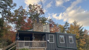 A two-story cabin with a stone chimney, a wooden deck, and a garage.
