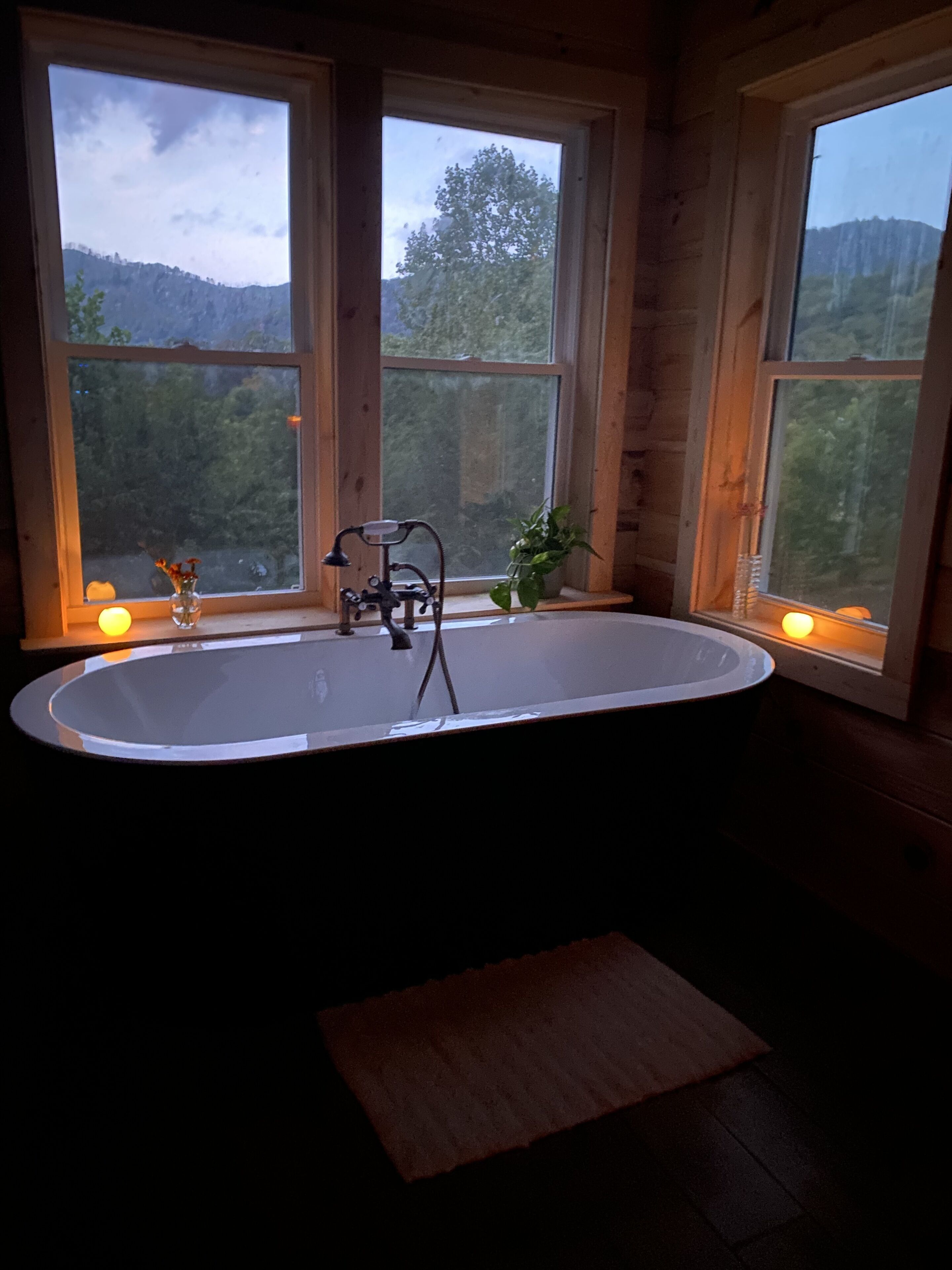 A bathroom with a freestanding bathtub, wooden walls, and large windows offering a view of a forested area.