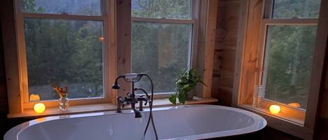 A bathroom with a freestanding bathtub, wooden walls, and large windows offering a view of a forested area.