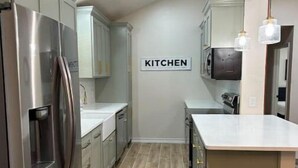 A modern kitchen with stainless steel appliances, light-colored cabinetry, and a 'KITCHEN' sign on the wall. - The CanyINN (Canyon)