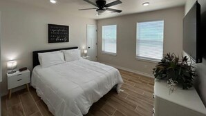 A bedroom with a bed, a ceiling fan, a wall-mounted TV, and a bedside table with a lamp. - The CanyINN (Canyon)