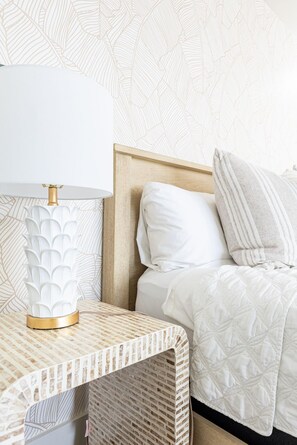 En pænt redt seng med hvid dyne og puder, et natbord med en lampe, og en væg med tapet.