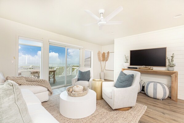 A modern living room with a white sofa, armchairs, a round coffee table, and a ceiling fan.