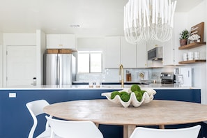 Una cocina moderna con armarios blancos, una isla central con encimera de madera y una lámpara colgante.
