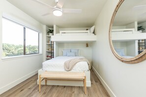 Une chambre avec un lit superposé, une table de chevet, un miroir et une fenêtre donnant sur les arbres.