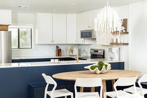 Une cuisine moderne avec des meubles blancs, un îlot central doté de sièges et un lustre.
