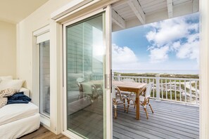 A room with a sliding glass door leading to a balcony with a view of the beach.