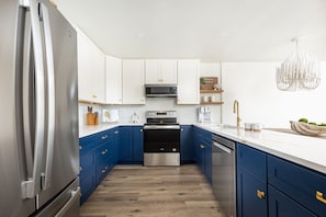 Une cuisine moderne dotée d’appareils électroménagers en acier inoxydable, de meubles de rangement bleus et d’un plan de travail blanc.