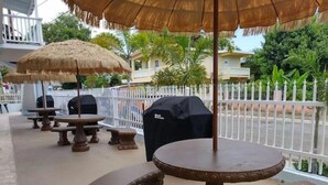 Terrasse mit Strohdächern, Grill und weißem Zaun.