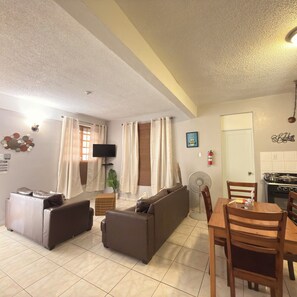 A living room with a sofa, a television, a dining table with chairs, and a kitchen area with a stove.