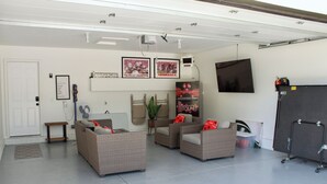 A spacious garage with a seating area featuring wicker furniture and a mounted television. - Husker Getaway
 (Lincoln)