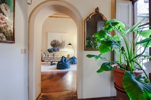 An interior hallway with a wooden floor, a potted plant, a mirror, and a doorway leading to another room.