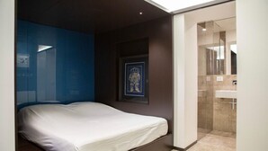 A bedroom with a bed, a framed picture on the wall, and a bathroom with a glass shower. - Luxury Suite Fori Imperiali (Roma)