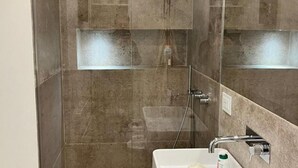 A modern bathroom with a glass-enclosed shower, a white sink, and a mirror. - Luxury Suite Fori Imperiali (Roma)