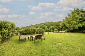 A grassy outdoor area with a table and chairs, surrounded by trees and bushes.