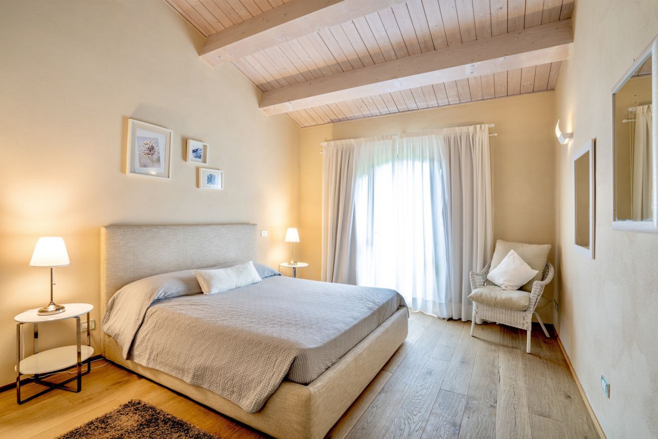 Un dormitorio con una cama grande, dos lámparas de noche, una silla y un ventanal con cortinas.