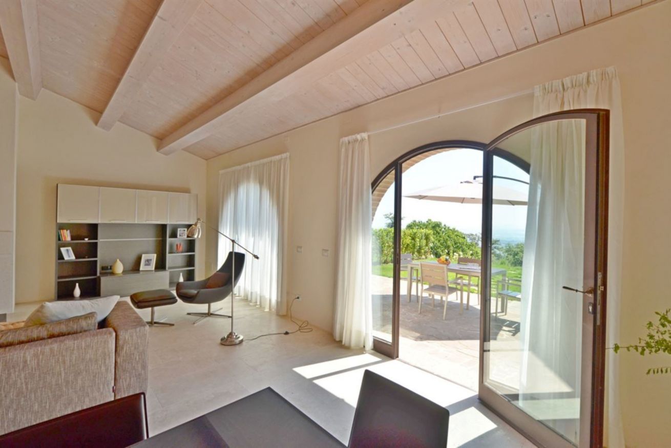 A modern living room with a sofa, a chair, a bookshelf, and a large sliding glass door leading to an outdoor patio.