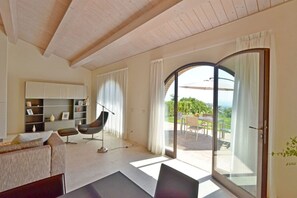 Ein modernes Wohnzimmer mit einer Couch, einem Sessel, einem Bücherregal und einem großen Schiebeglastür, die auf eine Terrasss führt.