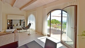 A modern living room with a sofa, a chair, a bookshelf, and a large sliding glass door leading to an outdoor patio.
