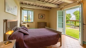 Un dormitorio con cama, mesita de noche, cómoda, ventana con vista al jardín y techo de madera.