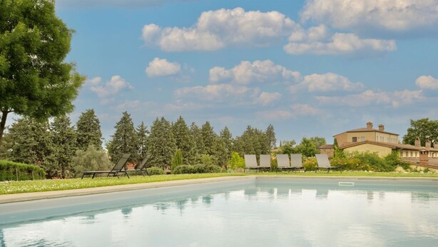 Una piscina con sillones de descanso, rodeada de árboles y un edificio al fondo.
