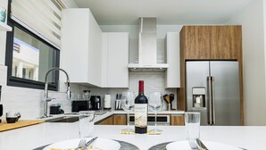 A modern kitchen with white cabinets, a stainless steel refrigerator, and a wine bottle on the counter. - Wariruri 2-07 Luxurious Apartment, private balcony! (Noord)