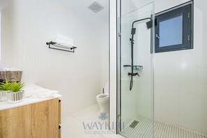 Un baño moderno con cabina de ducha de vidrio, inodoro blanco y tocador de madera con plantas.