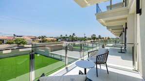 A balcony with a glass railing, a small table, and a chair with a cushion. - Wariruri 2-07 Luxurious Apartment, private balcony! (Noord)