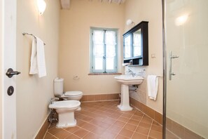 Une salle de bain avec deux toilettes, un lavabo, une fenêtre avec des rideaux et un espace douche.