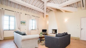 A spacious living room with a high ceiling, two sofas, a fireplace, and a television.