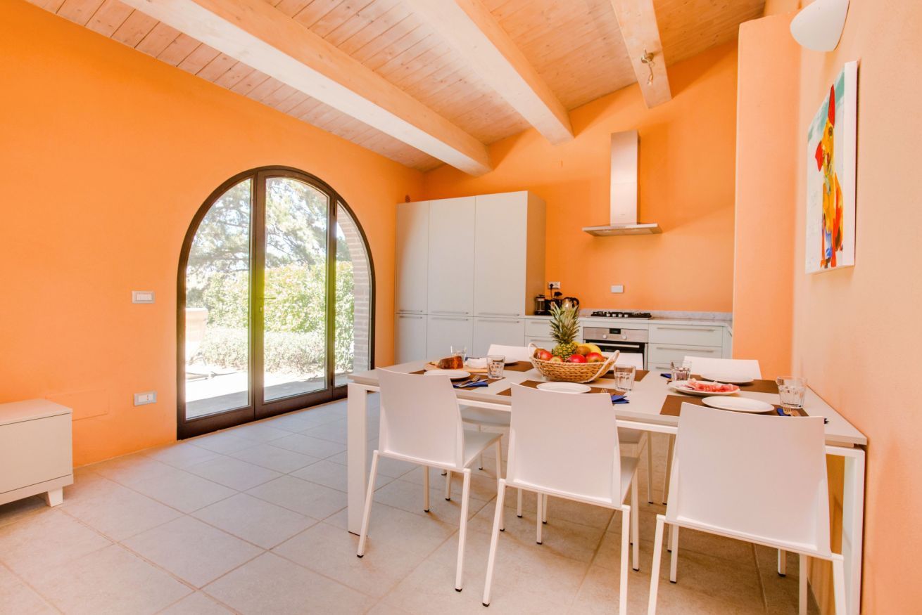 A bright kitchen with white cabinets, a dining table set for four, and a large window with a view of greenery.