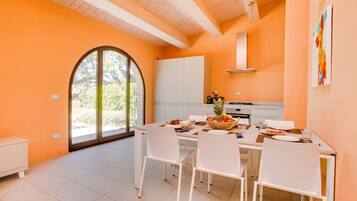 A bright kitchen with white cabinets, a dining table set for four, and a large window with a view of greenery.