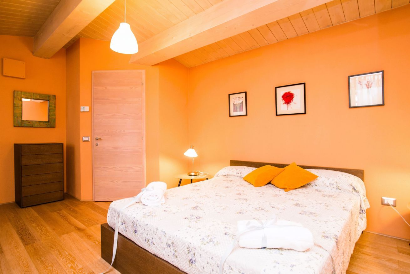 Una camera da letto con soffitto in legno, un letto con copripiumino floreale, due cuscini arancioni, un comodino con una lampada e una cassettiera in legno.