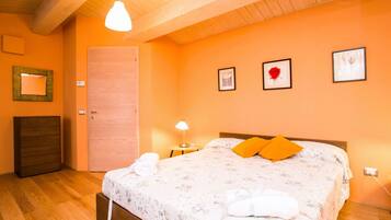 Una camera da letto con soffitto in legno, un letto con copripiumino floreale, due cuscini arancioni, un comodino con una lampada e una cassettiera in legno.