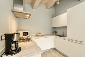 Une cuisine moderne avec des meubles blancs, un four à micro-ondes encastré, une machine à café et une cuisinière à gaz.