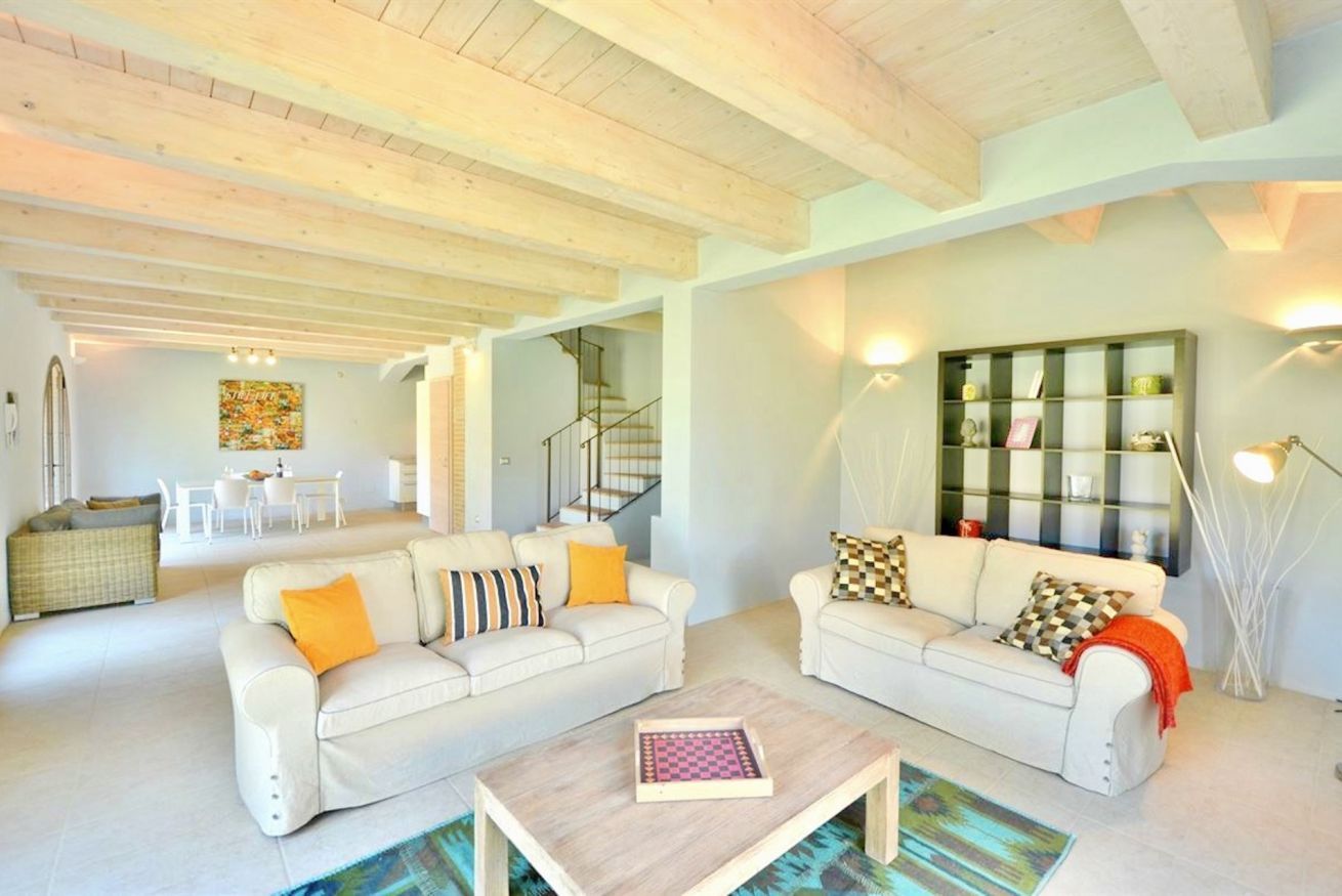 A spacious living area with two white sofas, a coffee table, and a staircase leading to an upper floor.