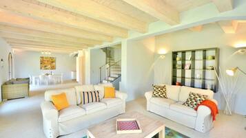 A spacious living area with two white sofas, a coffee table, and a staircase leading to an upper floor.