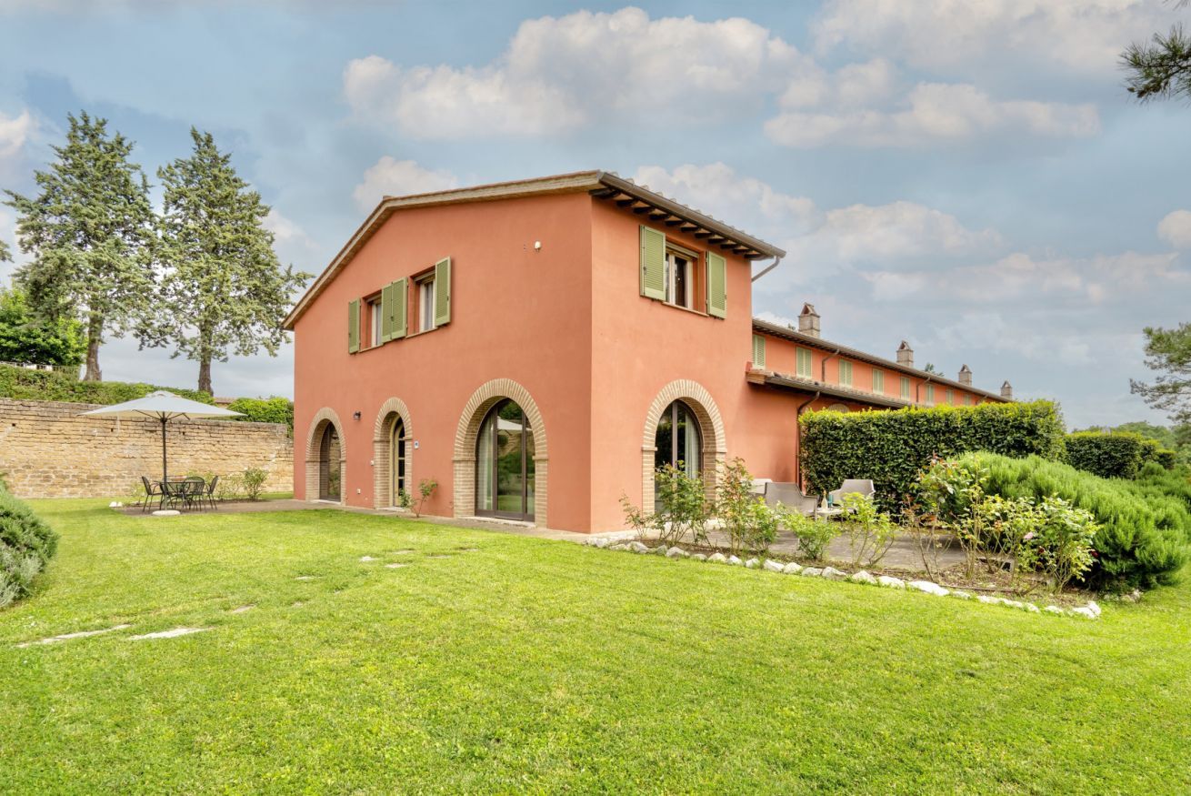 A two-story house with a red facade, green shutters, and a well-maintained lawn.