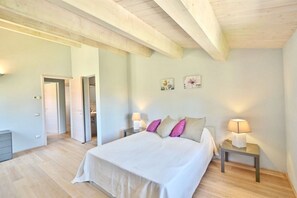 A bedroom with a large bed, two bedside tables with lamps, a wooden ceiling, and a door leading to another room. - Elegant and spacious two-storey villa of 142 m2 composed on the ground floor of a large living room, kitchen complete with dishwasher, microwave oven, electric oven, coffee machine, kettle, fridge and freezer.On the first floor we find a double bedroom w (Trequanda)