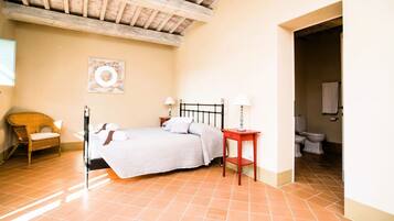 A bedroom with a bed, bedside tables, a chair, and a bathroom visible through an open doorway.