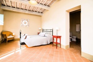 A bedroom with a bed, bedside tables, a chair, and a bathroom visible through an open doorway. - Elegant ground floor apartment of 92 m2, composed of a large living room with fireplace, kitchen complete with dishwasher, microwave oven, electric oven, coffee machine, kettle, fridge and freezer, internal and external dining area, a double bedroom with (Trequanda)