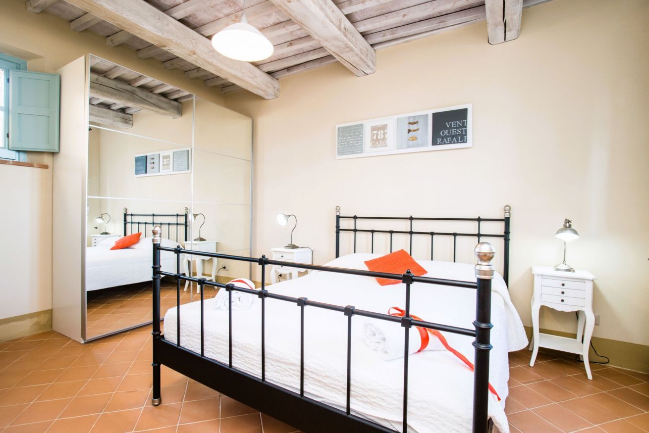 Een slaapkamer met een bed, nachtkastjes, een spiegel en een plafond met zichtbare balken.