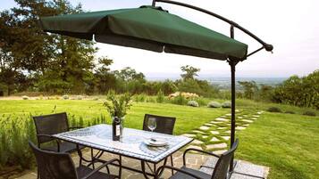 A patio with a table and chairs, a green umbrella, and a view of a landscaped garden.