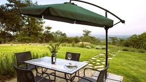 Une terrasse avec une table et des chaises, un parasol vert et une vue sur un jardin aménagé.
