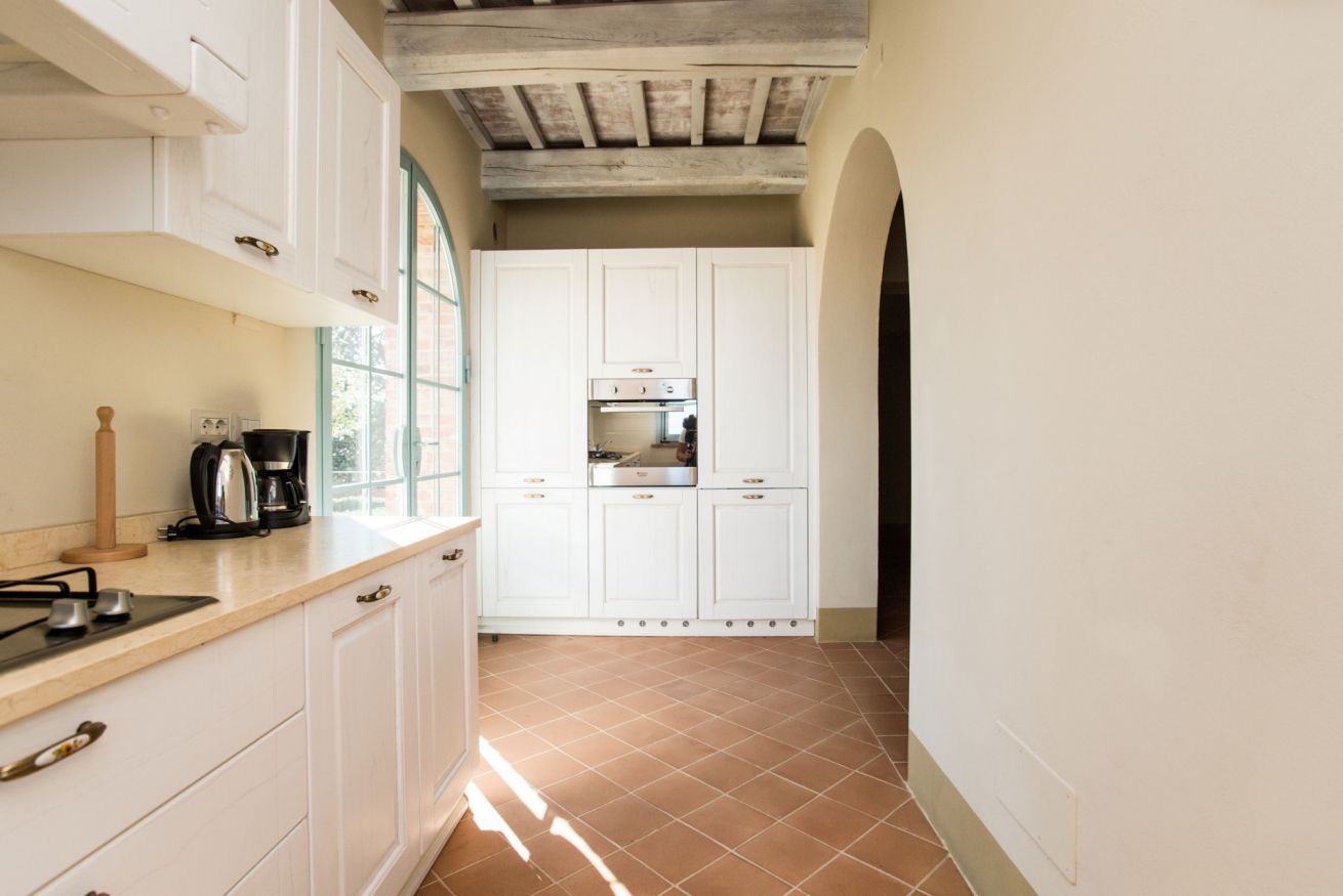 Een keuken met witte kastjes, een betegelde vloer en een raam dat natuurlijk licht binnenlaat.