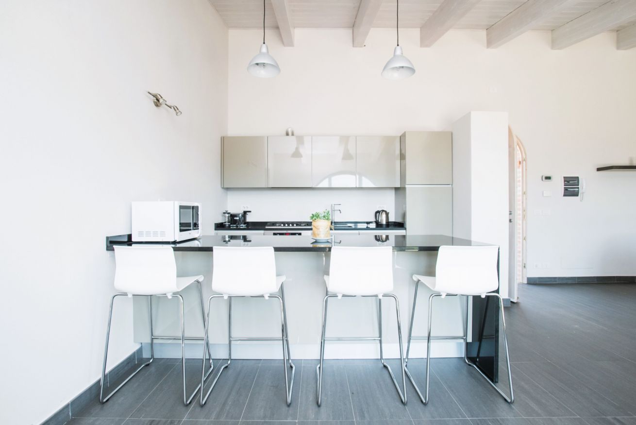 Een moderne keuken met witte kasten, een zwart aanrecht en vier witte barkrukken.