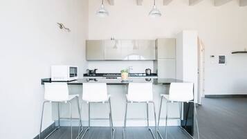 Een moderne keuken met witte kasten, een zwart aanrecht en vier witte barkrukken.