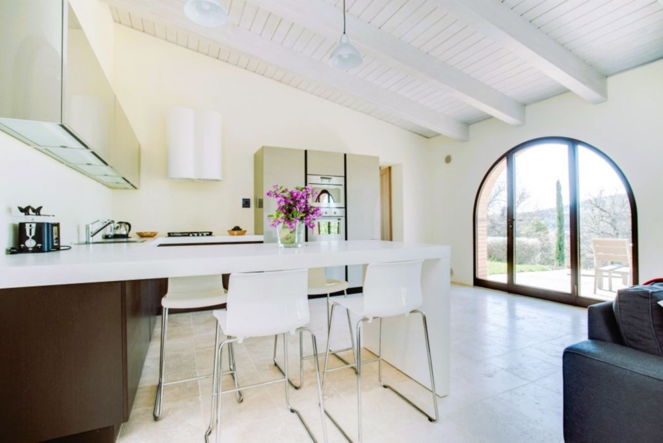 A modern kitchen with a white countertop, bar stools, and a large window.