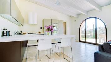 A modern kitchen with a white countertop, bar stools, and a large window.